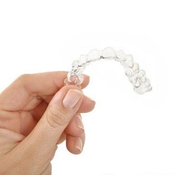 A person is holding a clear aligner in their hand.