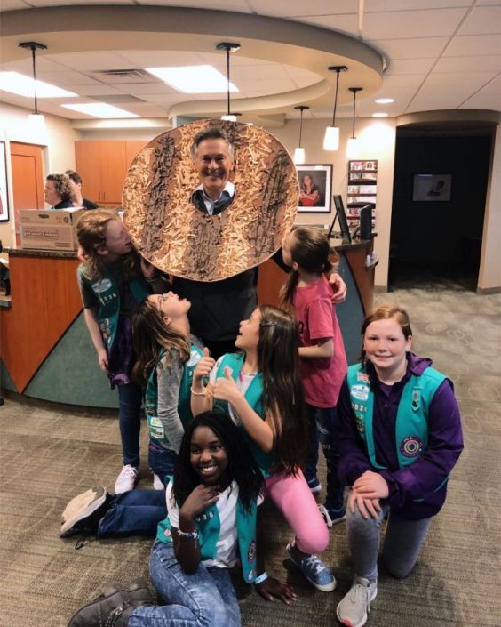 A group of girl scouts posing for a picture with a man in a donut costume