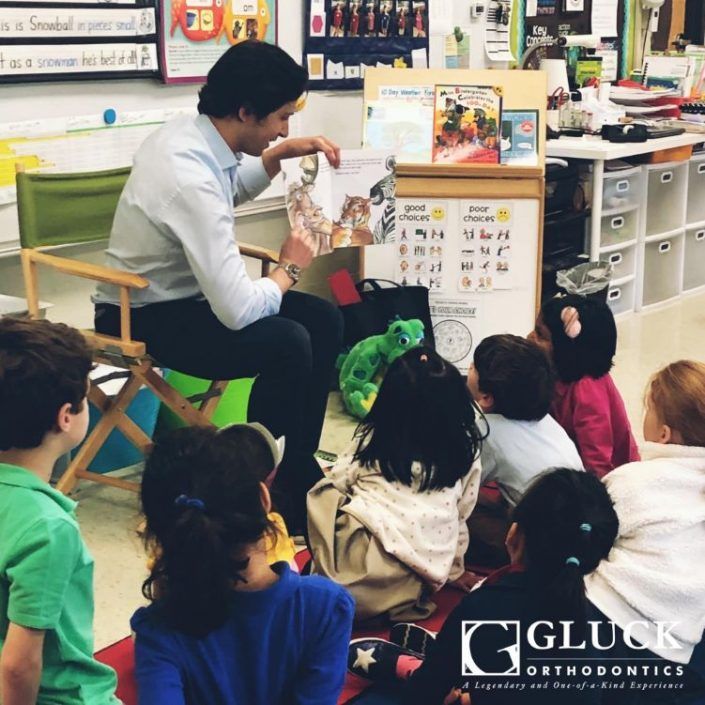 A man is reading a book to a group of children sponsored by gluck orthodontics