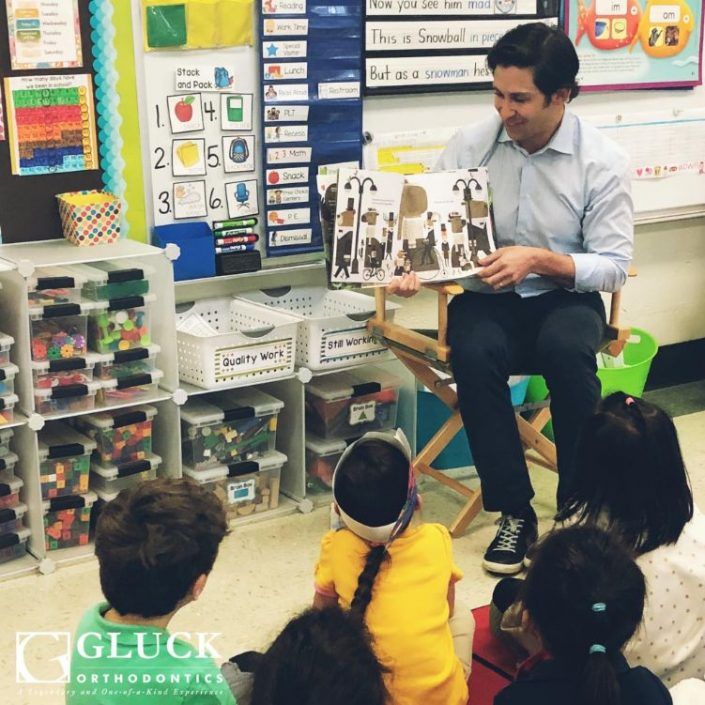 A man sits in a chair reading a book to a group of children
