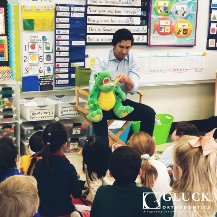 A man is sitting in front of a group of children holding a stuffed frog