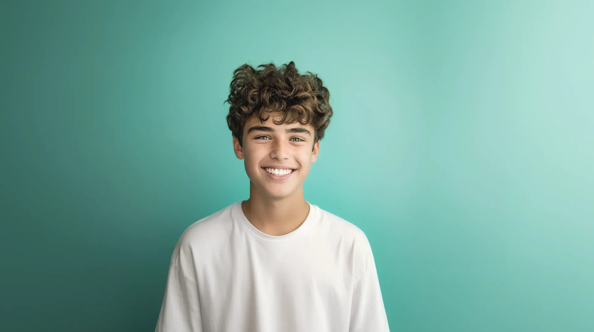 A young man with curly hair is smiling against a blue background.