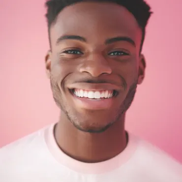 A young man with a beard is smiling in front of a pink background.