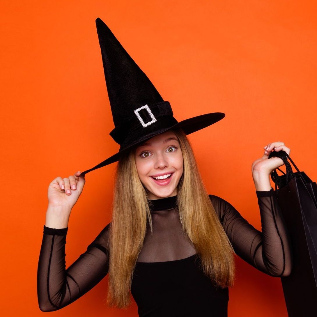 A woman is wearing a witch hat and holding a shopping bag.