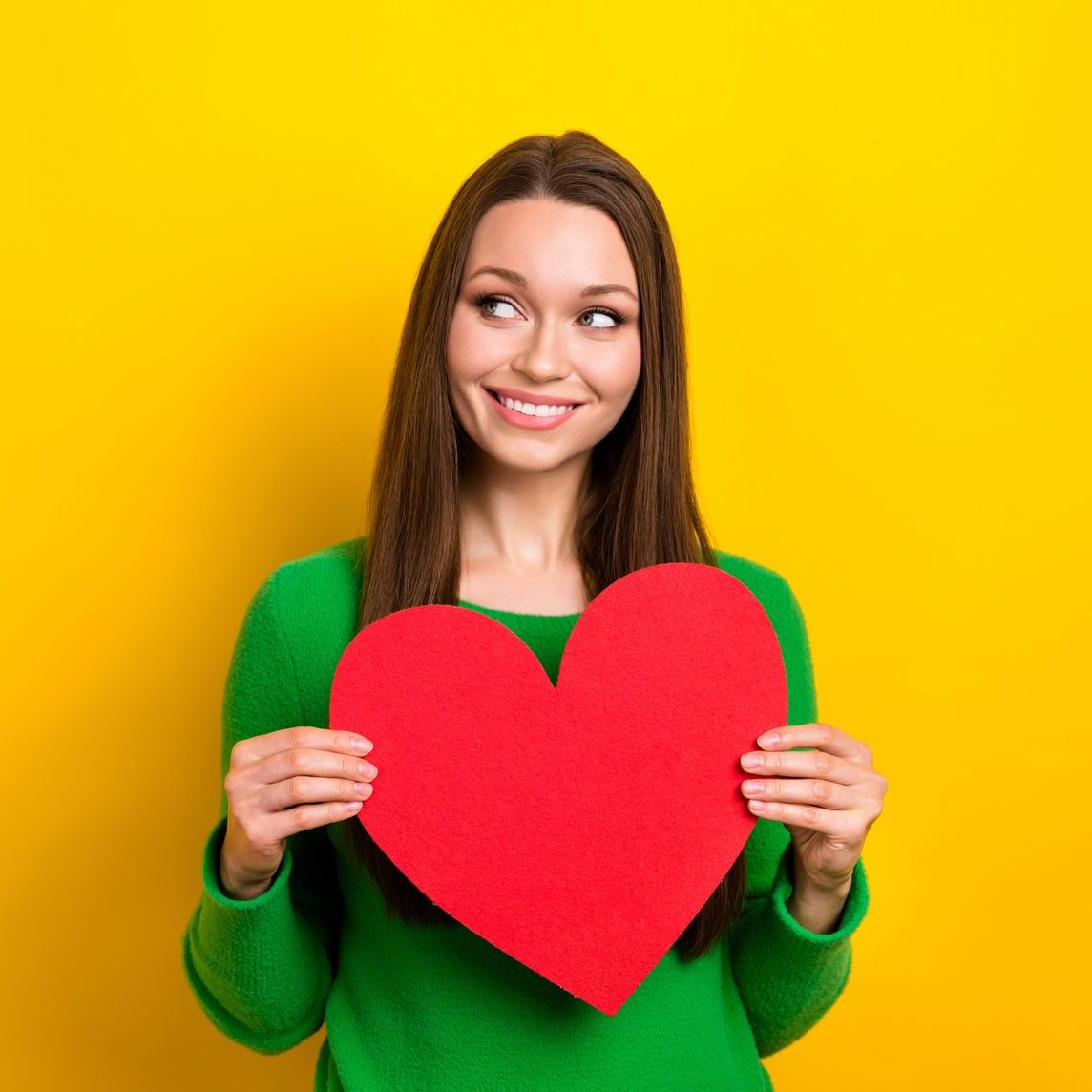 A woman in a green sweater is holding a red heart.