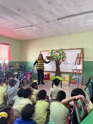 A person in a bee costume presents to children in a classroom with a tree prop.