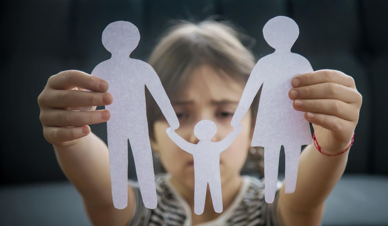 Child holding paper cutouts of a family, looking sad.