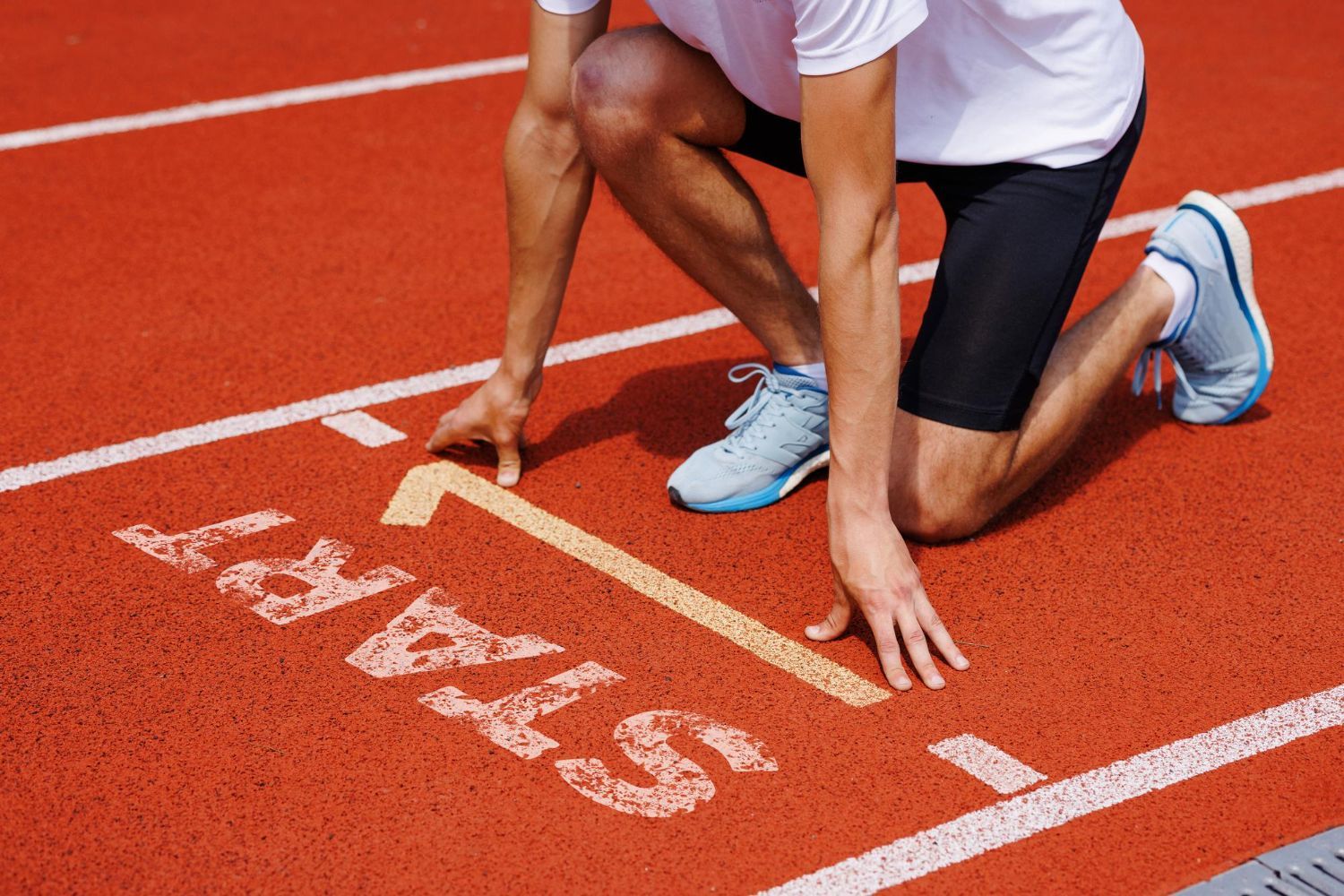 Runner at the starting line of a track, hands down, ready to begin.