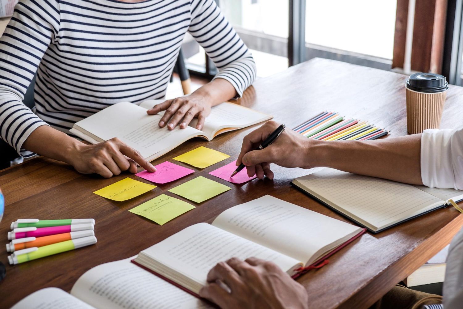 People studying at a table with books, sticky notes, and colored pens.