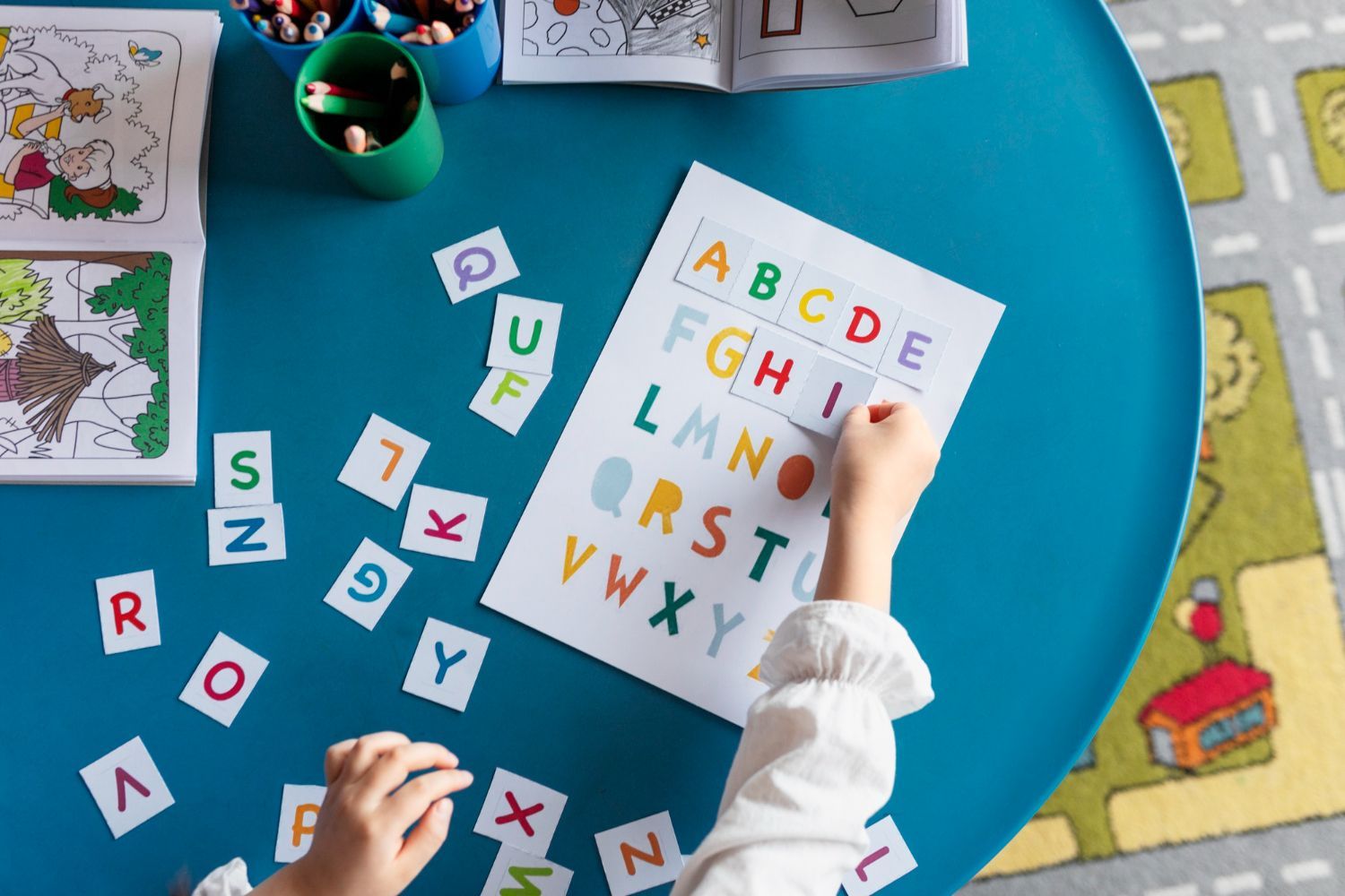 A child's hands pointing at a colorful alphabet chart and letter cutouts on a blue table.