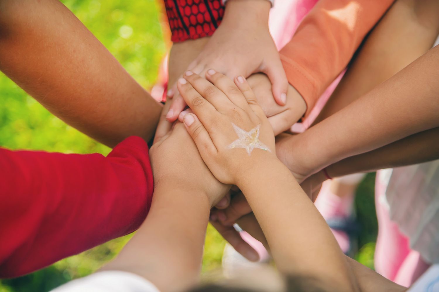 Hands of multiple people stacked in a close circle. One hand has a star drawn on it.