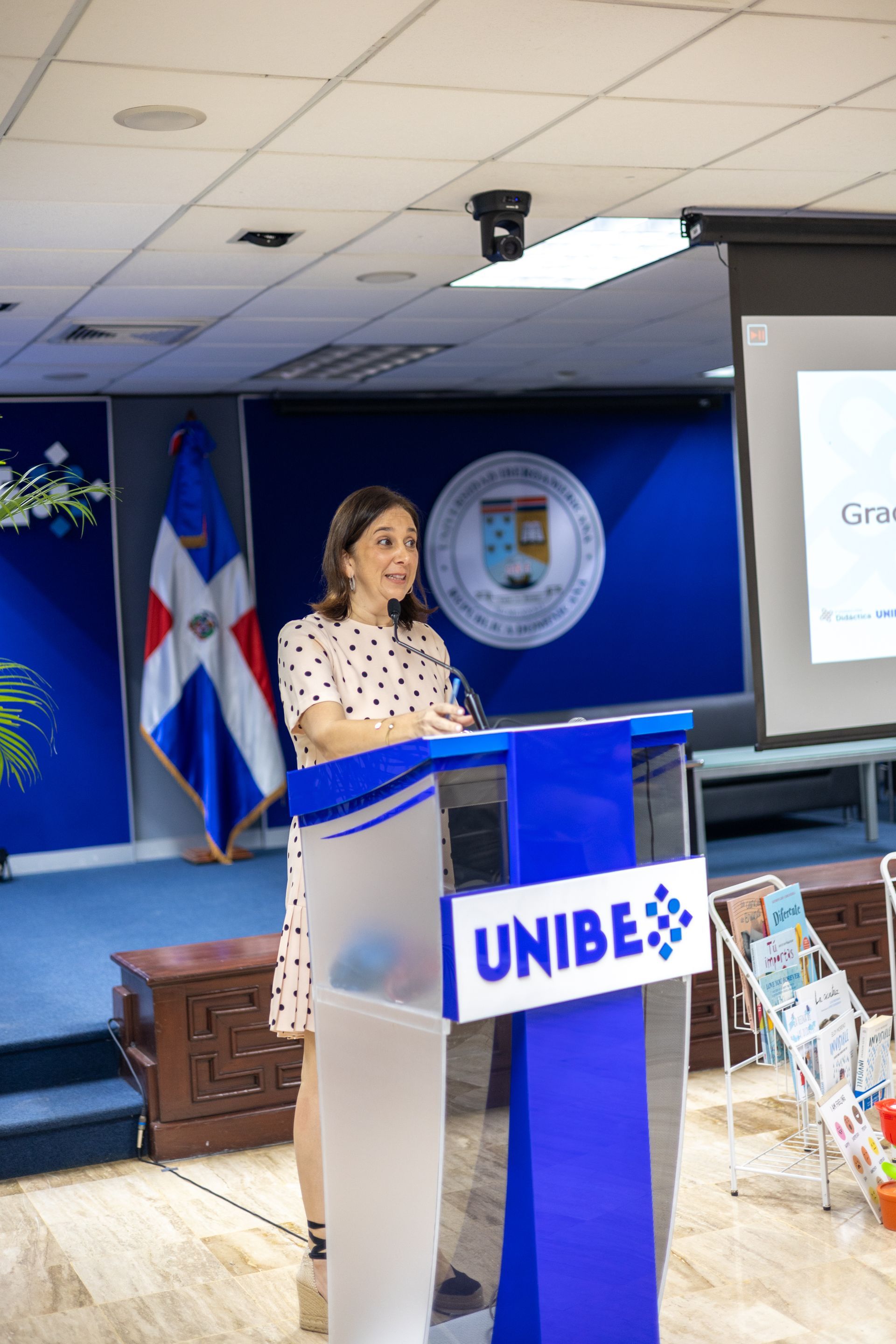 Woman speaking at a podium with UNIBE logo, Dominican Republic flag in background.