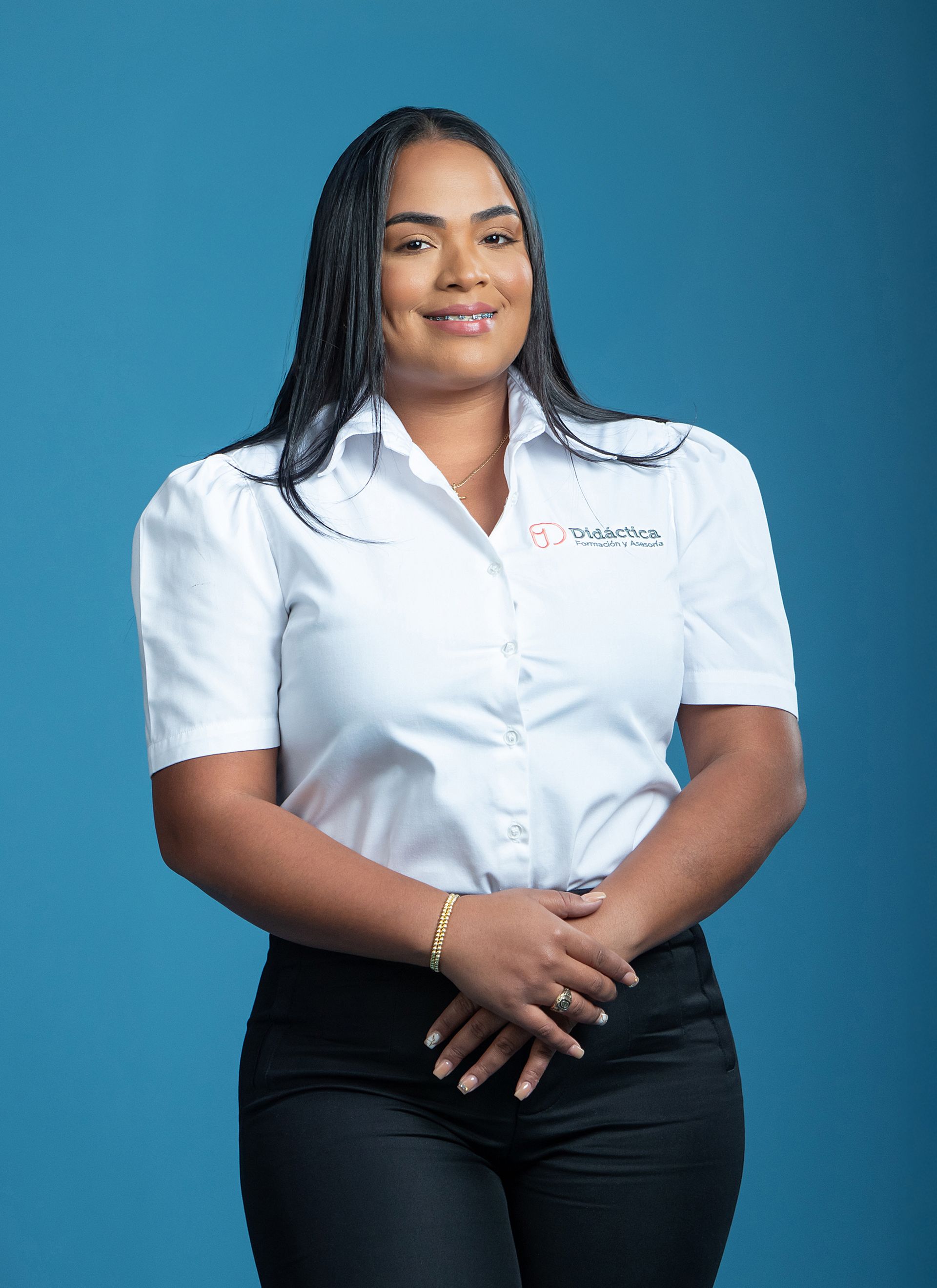 Woman in white button-up and black pants, arms crossed, smiling. Blue backdrop.