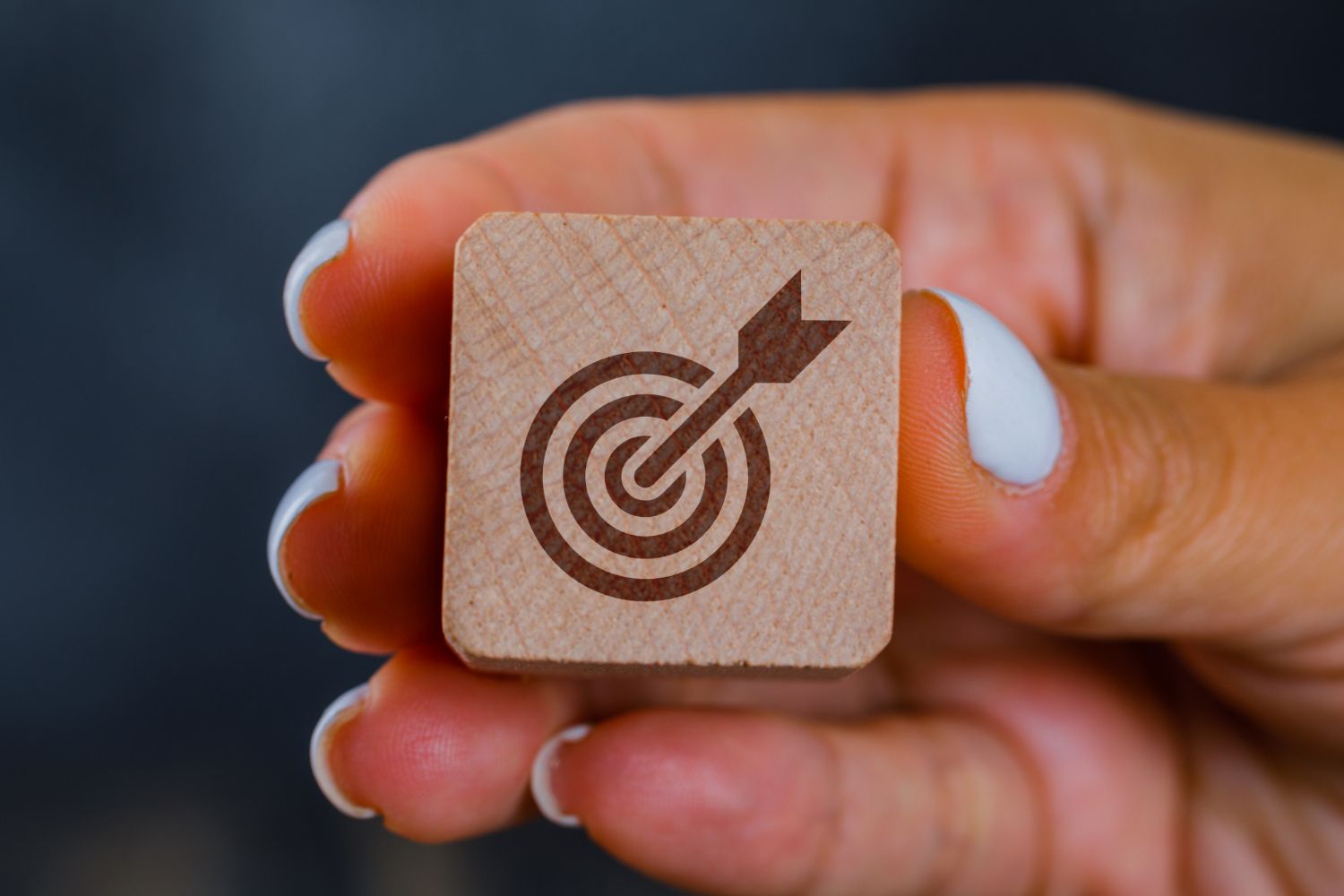Hand holding a wooden block with a target and arrow symbol.
