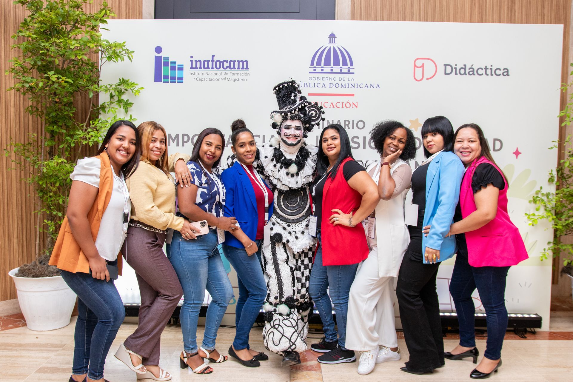 Group of people posing with a costumed mime in front of a banner with logos.