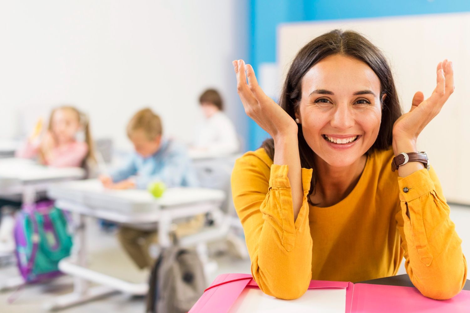 Woman smiling, raising hands, in classroom with students.