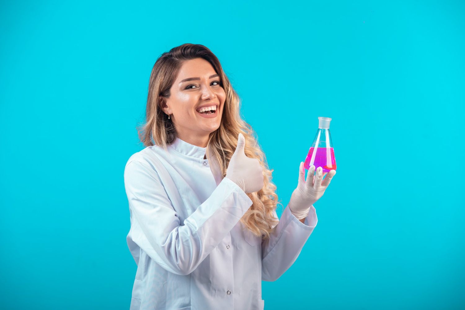 Woman in lab coat holding a flask of pink liquid, giving thumbs up. Blue background.