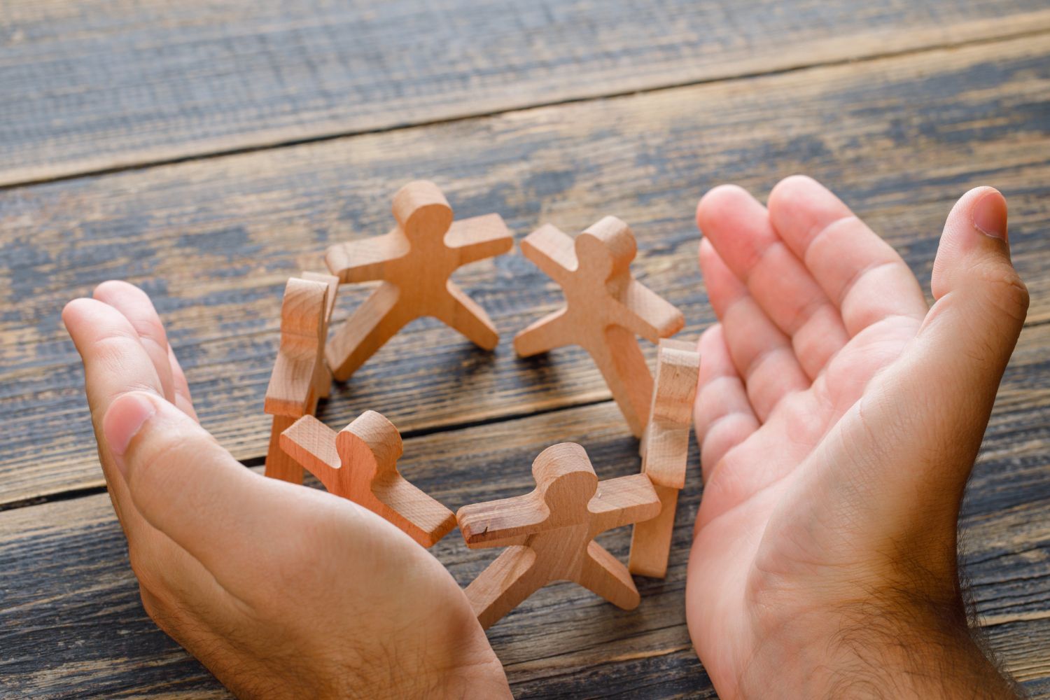 Hands cupping a circle of wooden figures.