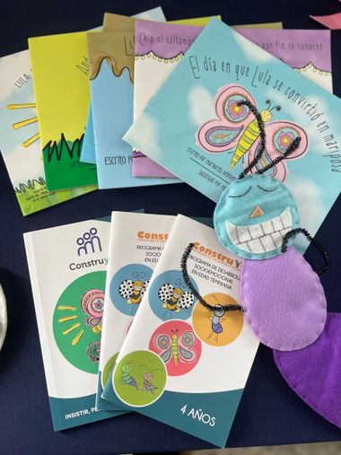 Books and a stuffed butterfly on a table; colorful covers, some with Spanish text.