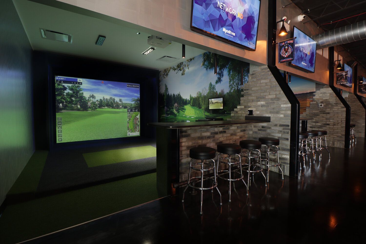 A golf simulator with a lot of televisions on the wall.