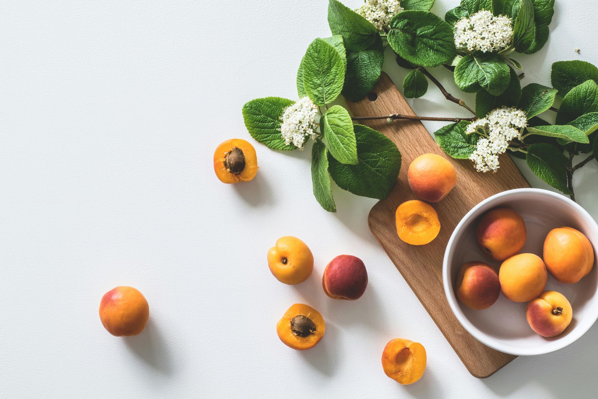 A bowl of apricots next to a cutting board and flowers.