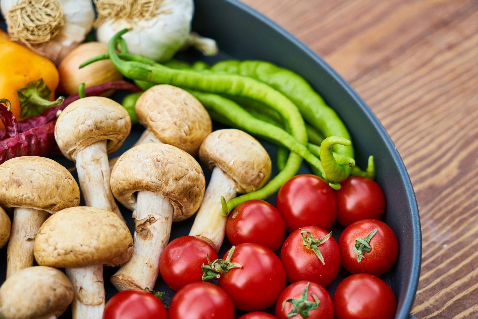 A pan filled with mushrooms , tomatoes , peppers and garlic on a wooden table.