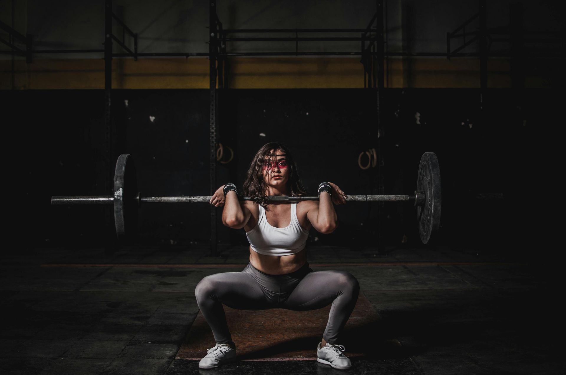 A woman is squatting with a barbell over her head in a gym.