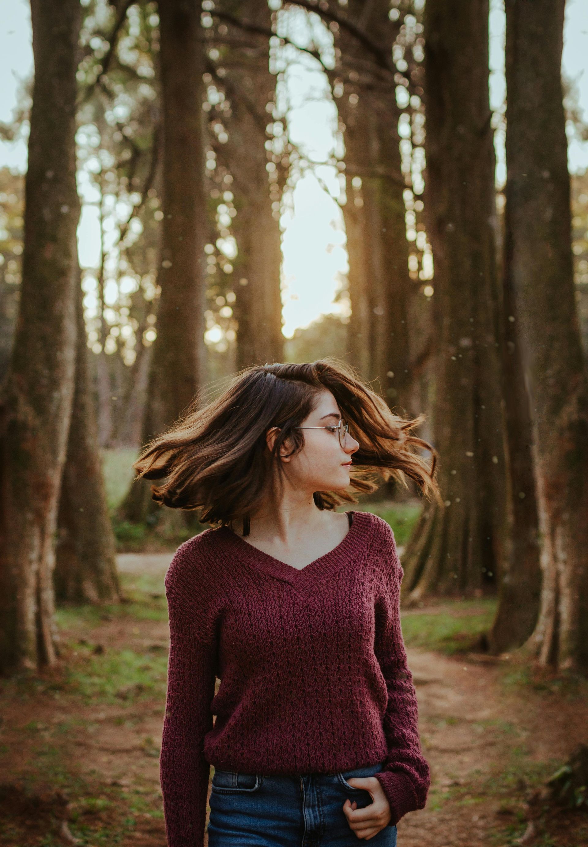 A woman in a sweater is standing in the middle of a forest.