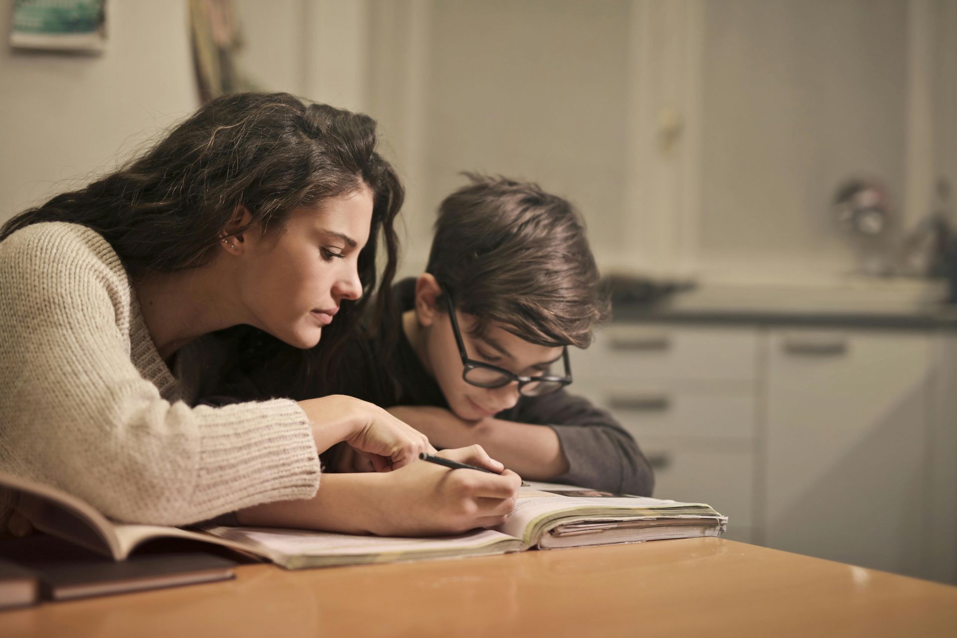 A woman is helping a boy with his homework at a table.