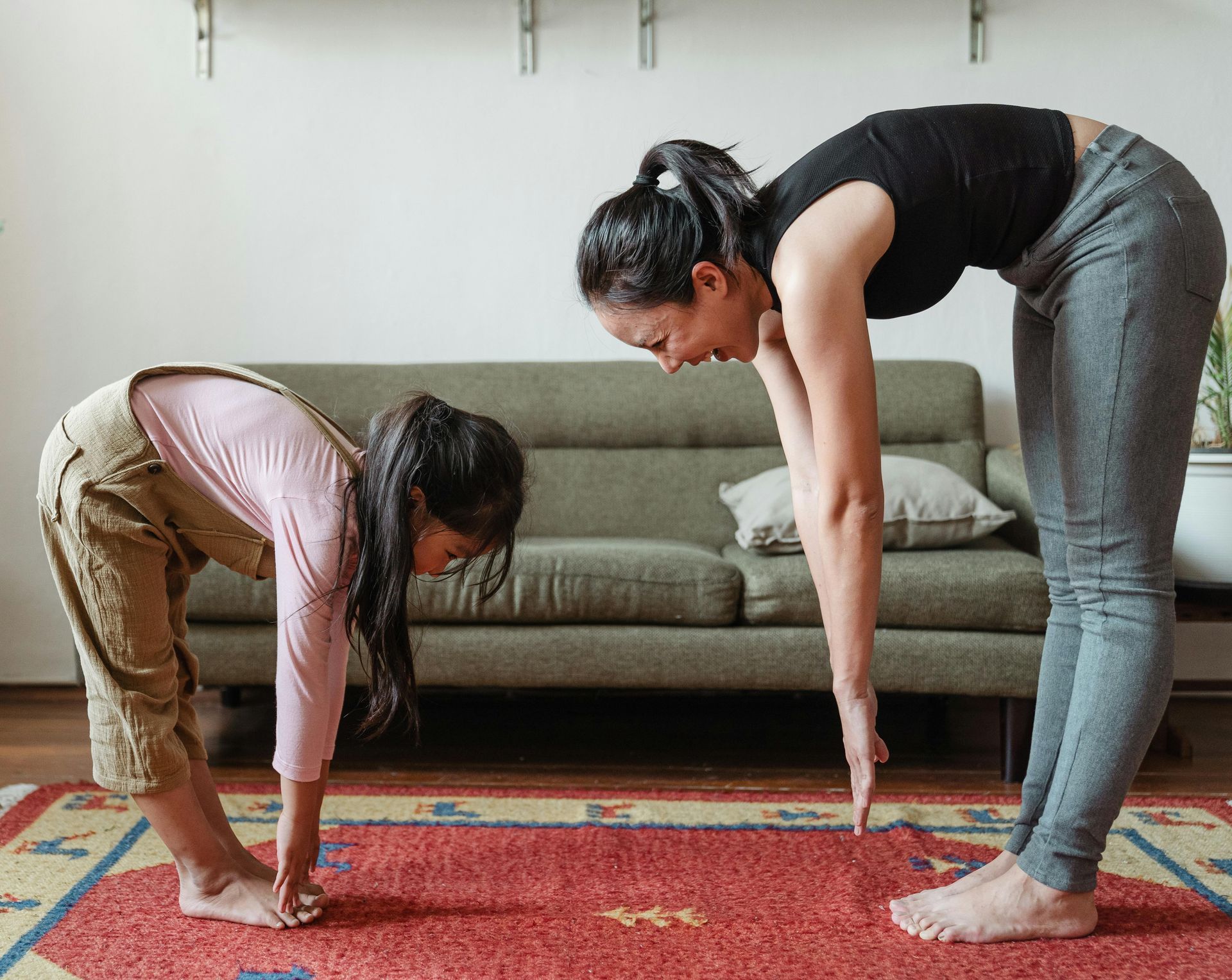 A woman and a little girl are doing yoga together in a living room.