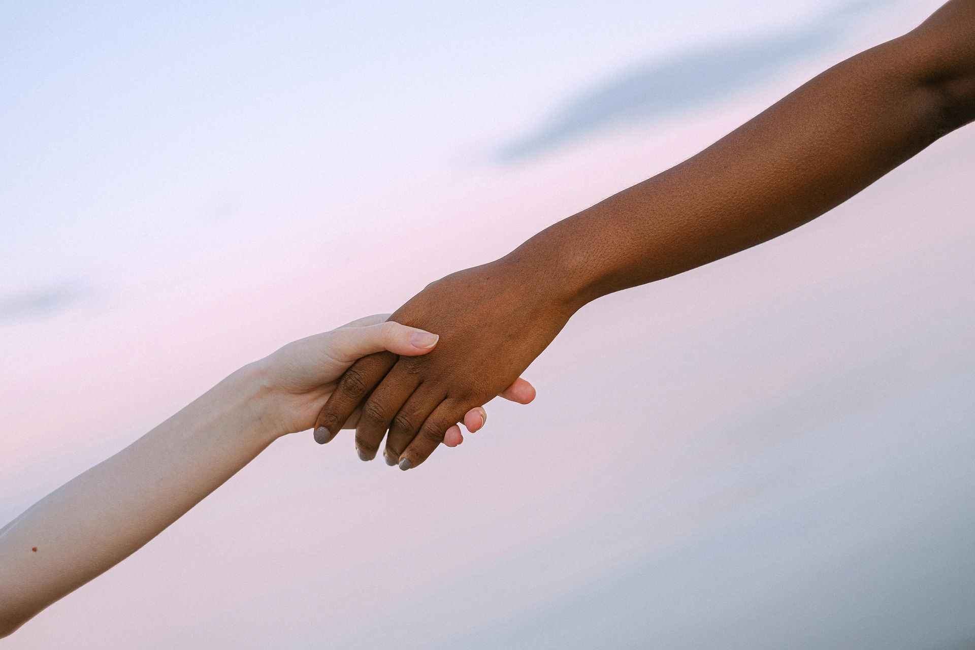 Two people are holding hands in front of a body of water.