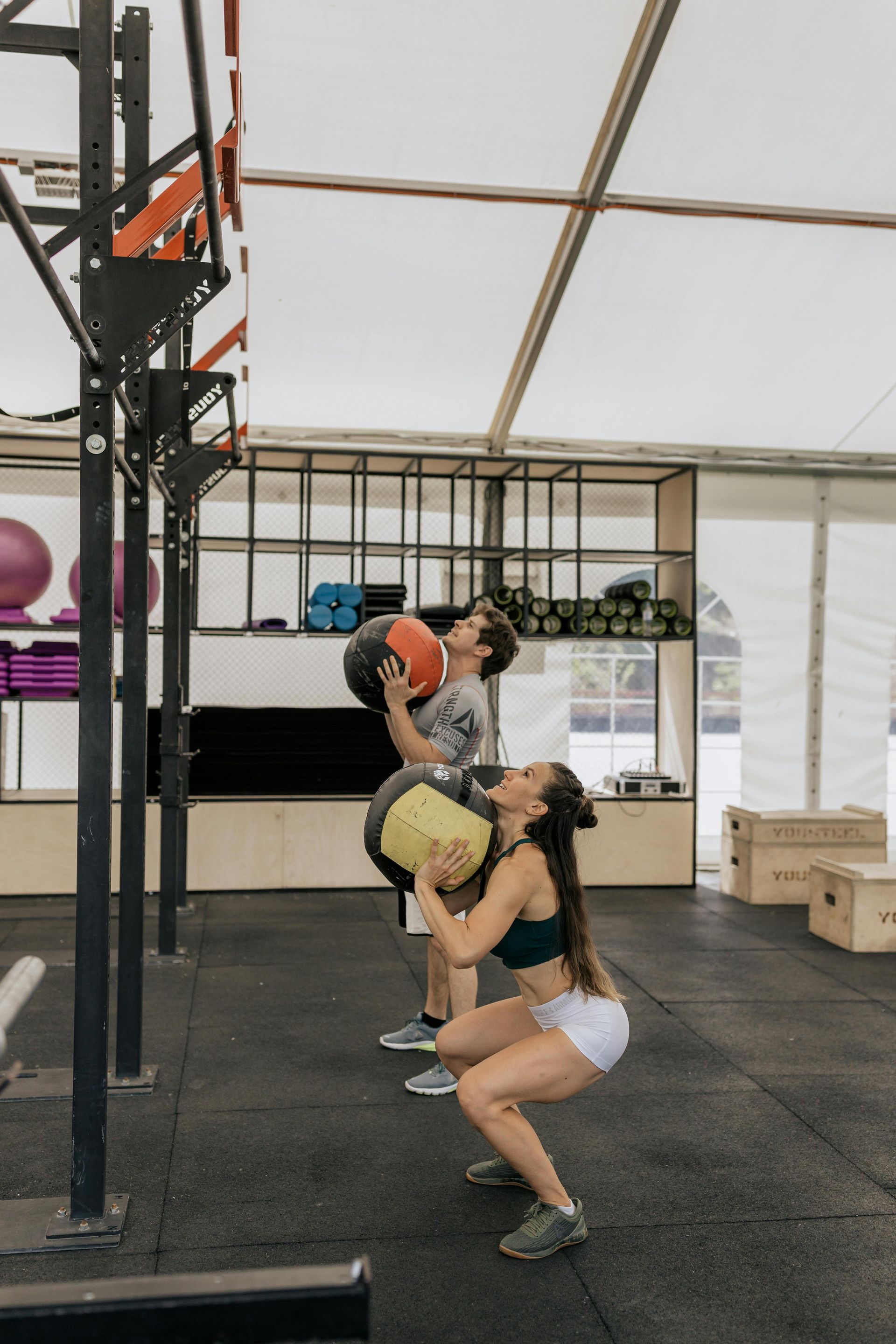A man and a woman are squatting in a gym while holding weights.