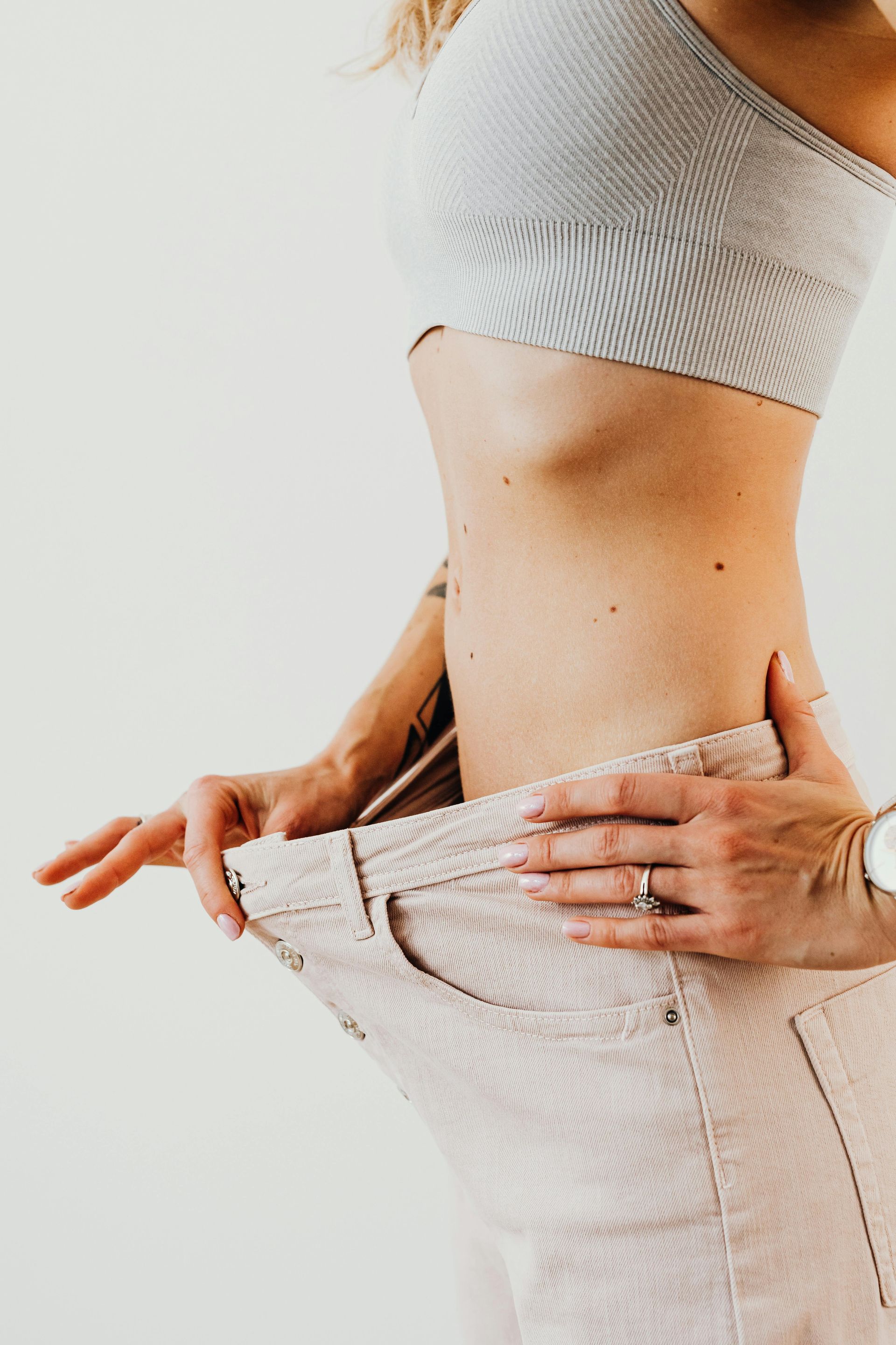 A woman in a crop top and jeans is measuring her waist.