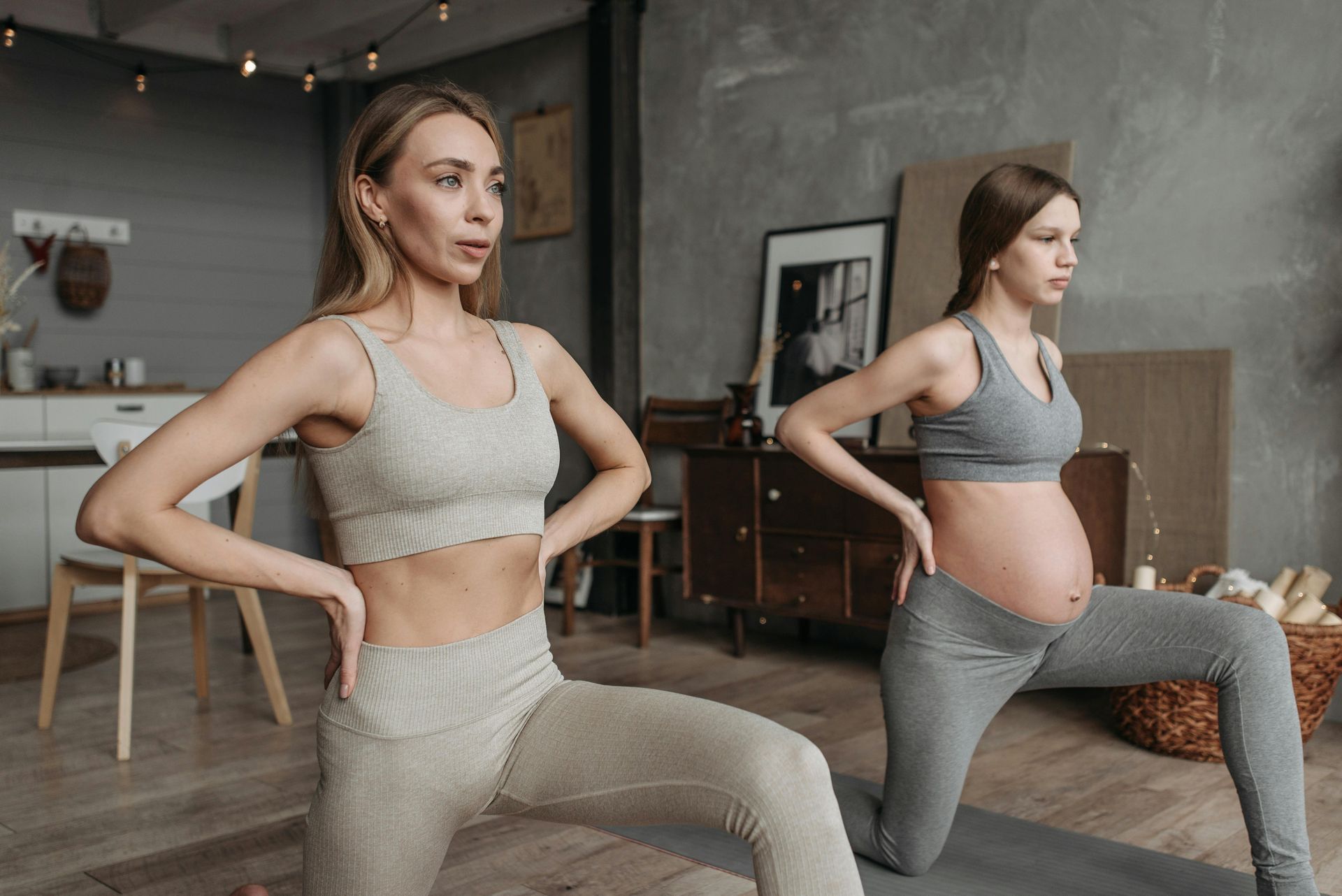 Two pregnant women are doing yoga together in a living room.