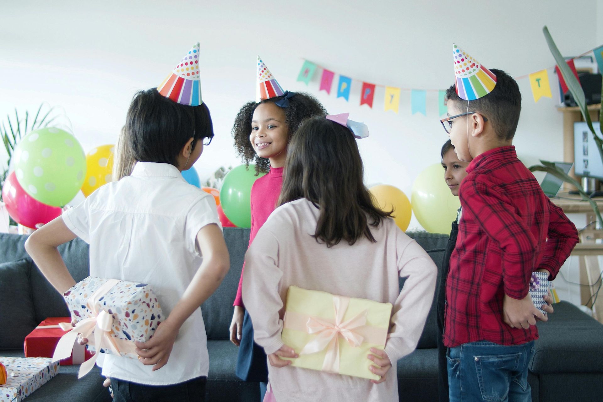 A group of children are standing around a couch at a birthday party.