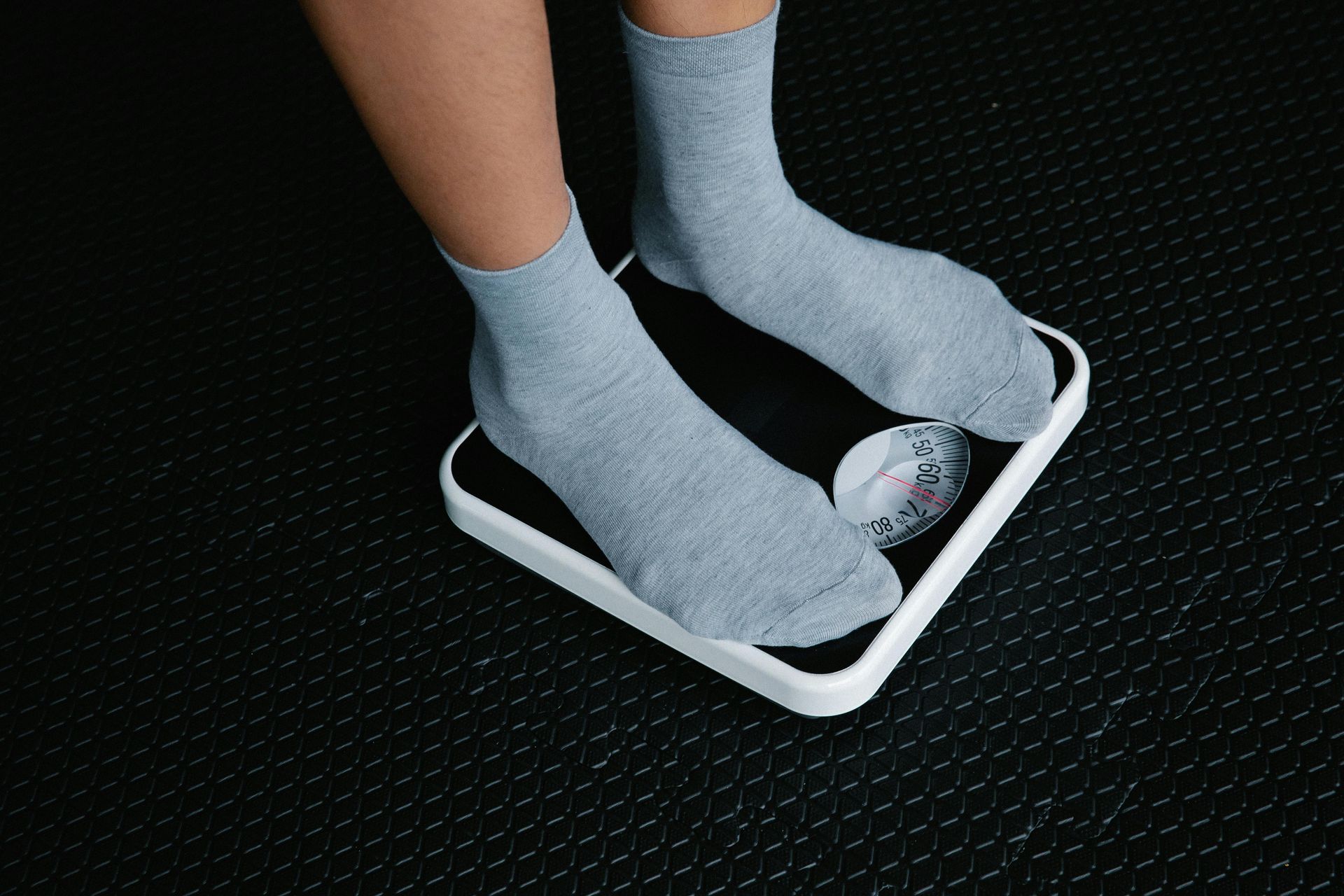 Person standing on a digital bathroom scale in gray socks on a black floor.