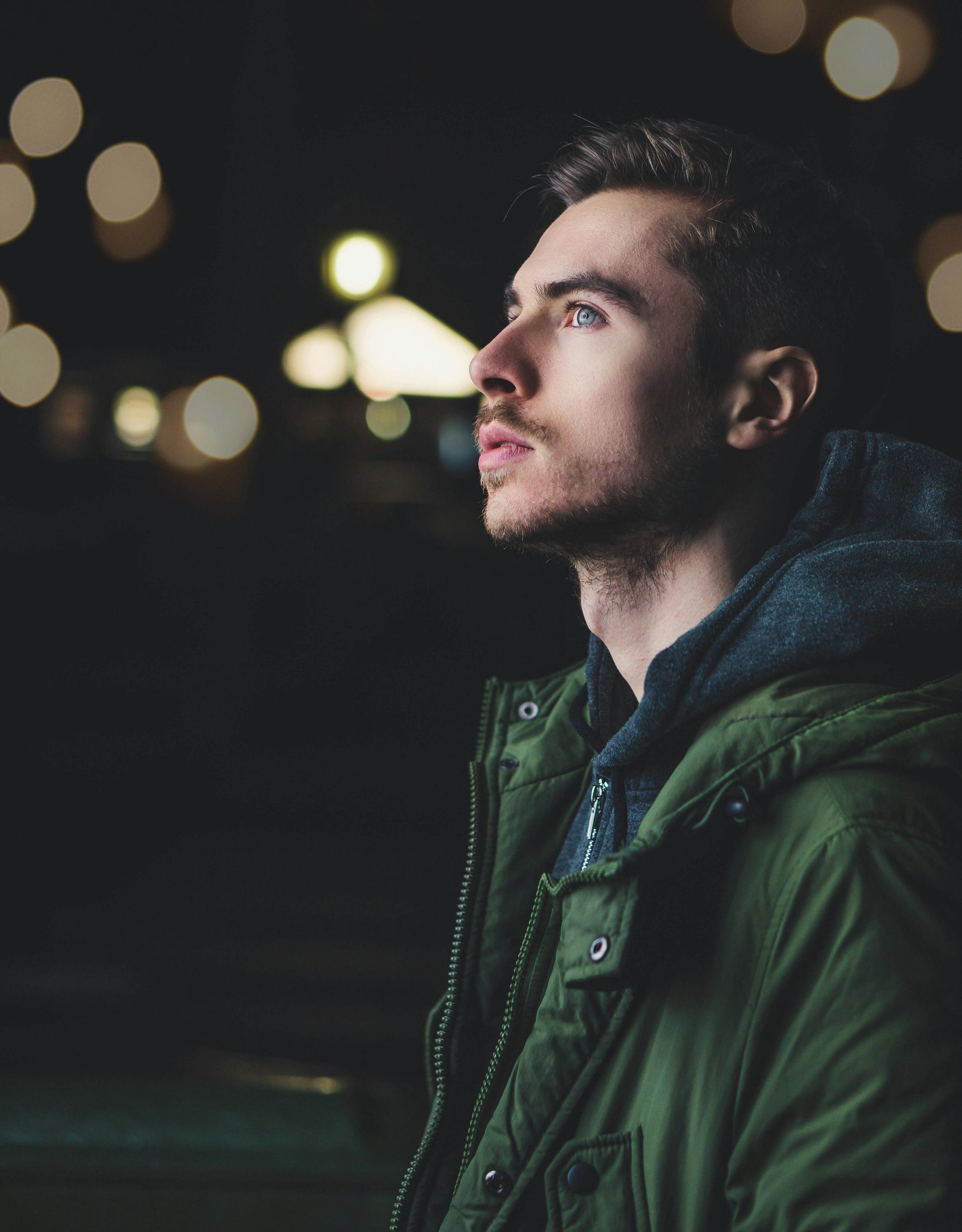 A man in a green jacket is looking up at the sky at night.