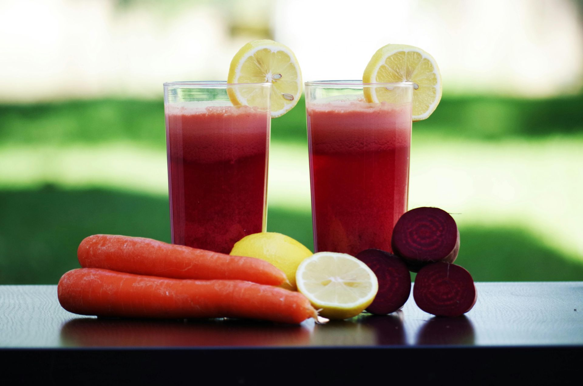 Two glasses of juice with carrots , lemons and beets on a table.