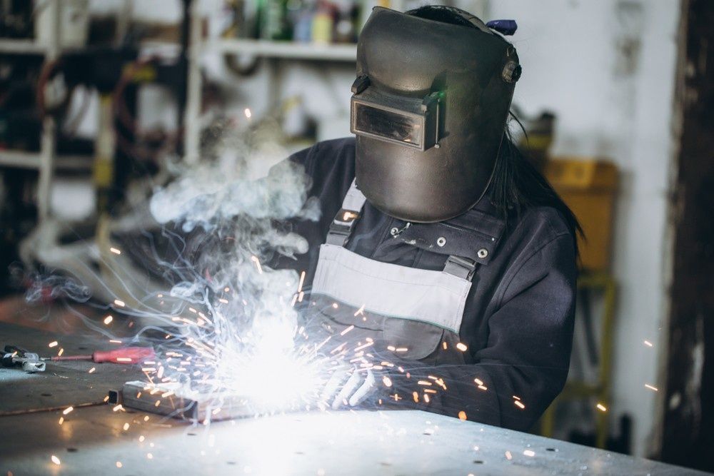 A Woman is Welding a Piece of Metal in a Garage — FNQ Filters & Parts In Mareeba, QLD