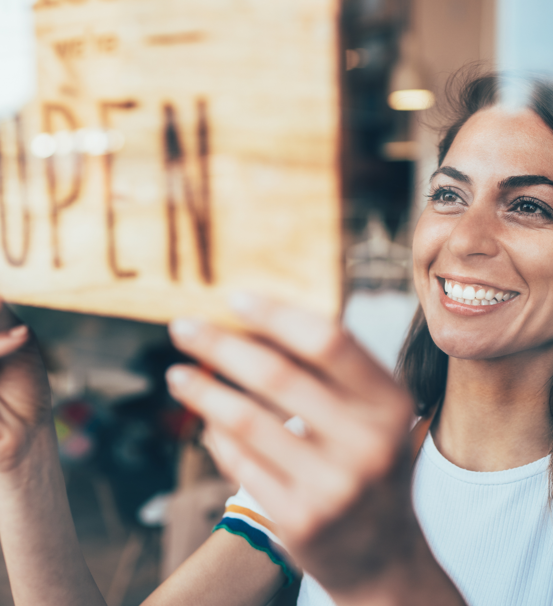 A woman is smiling while holding an open sign