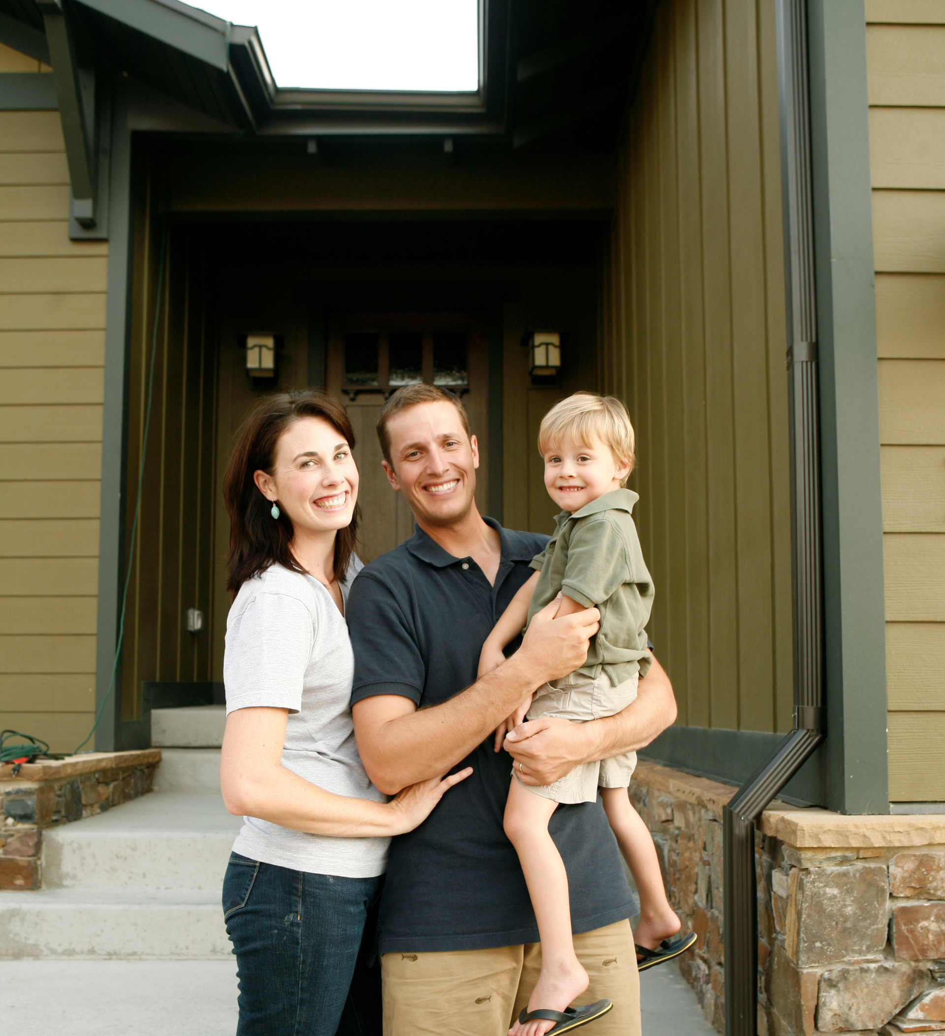 A man and woman are holding a child in front of a house.