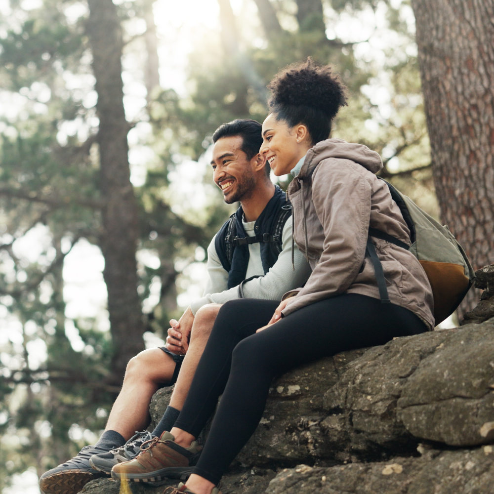 A man and a woman are sitting on a rock in the woods.