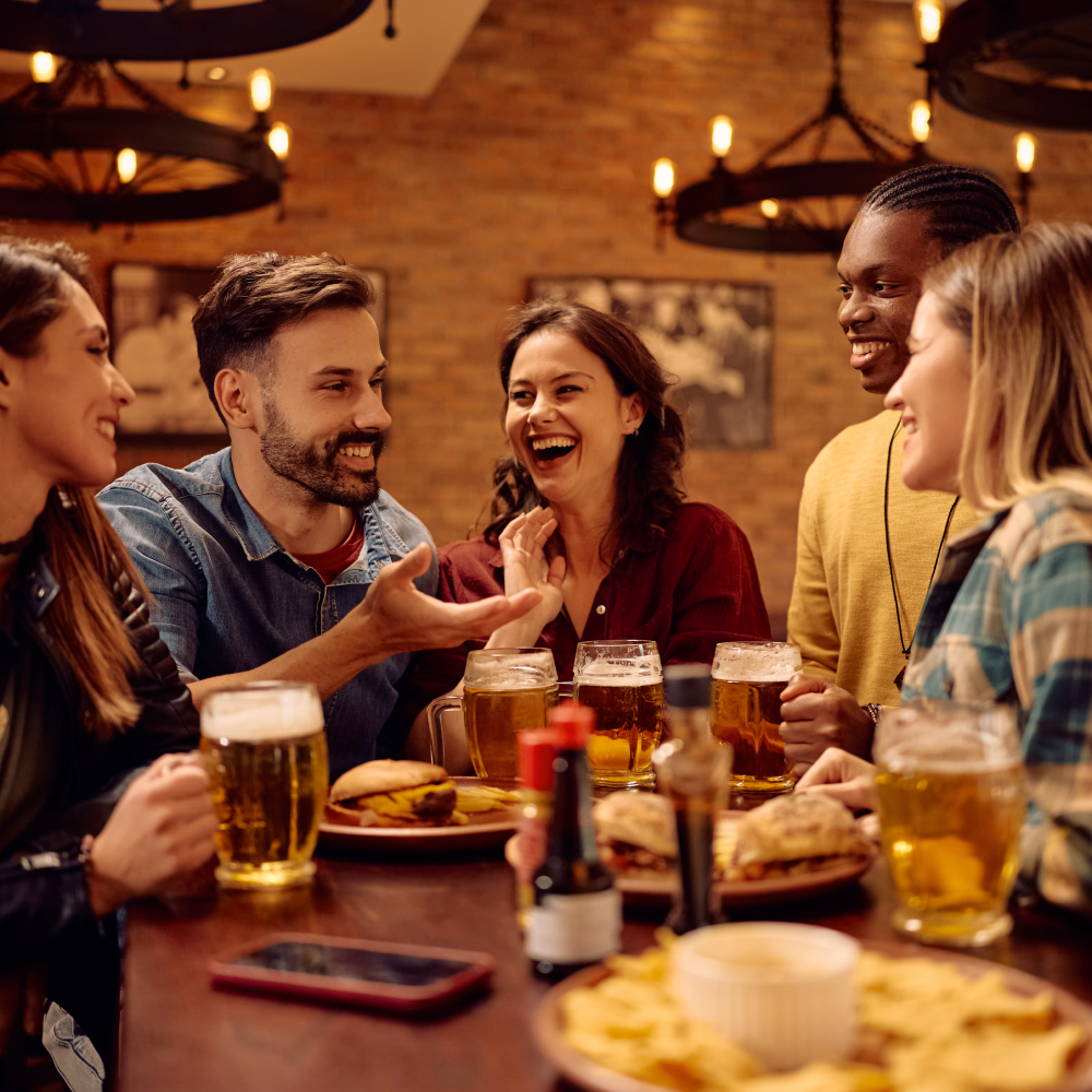 A group of people are sitting around a table eating food and drinking beer.