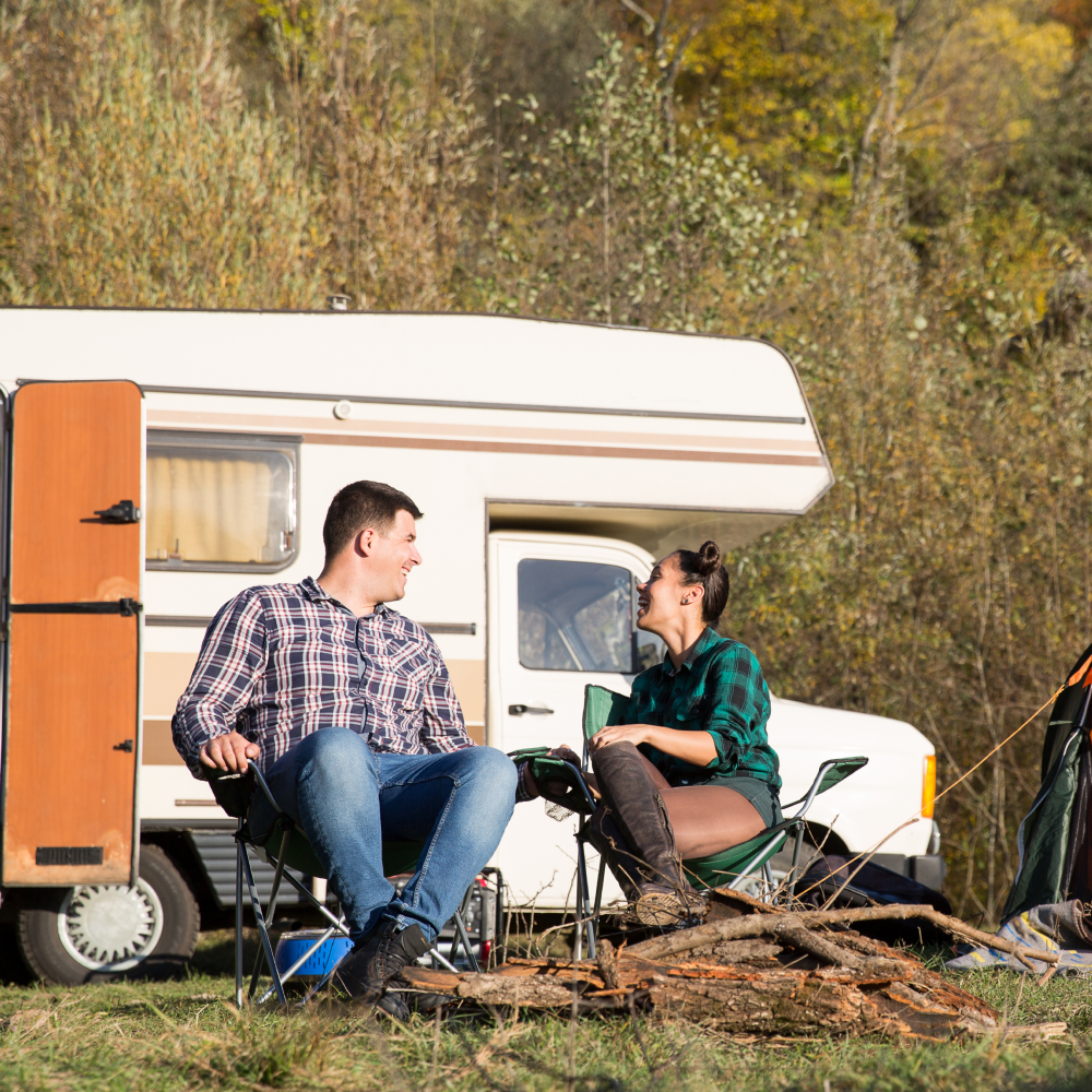 A man and a woman are sitting in chairs in front of a rv.