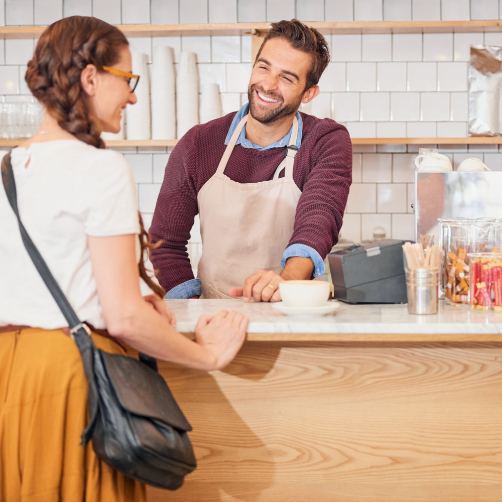 A man in an apron is talking to a woman at a counter in a restaurant.