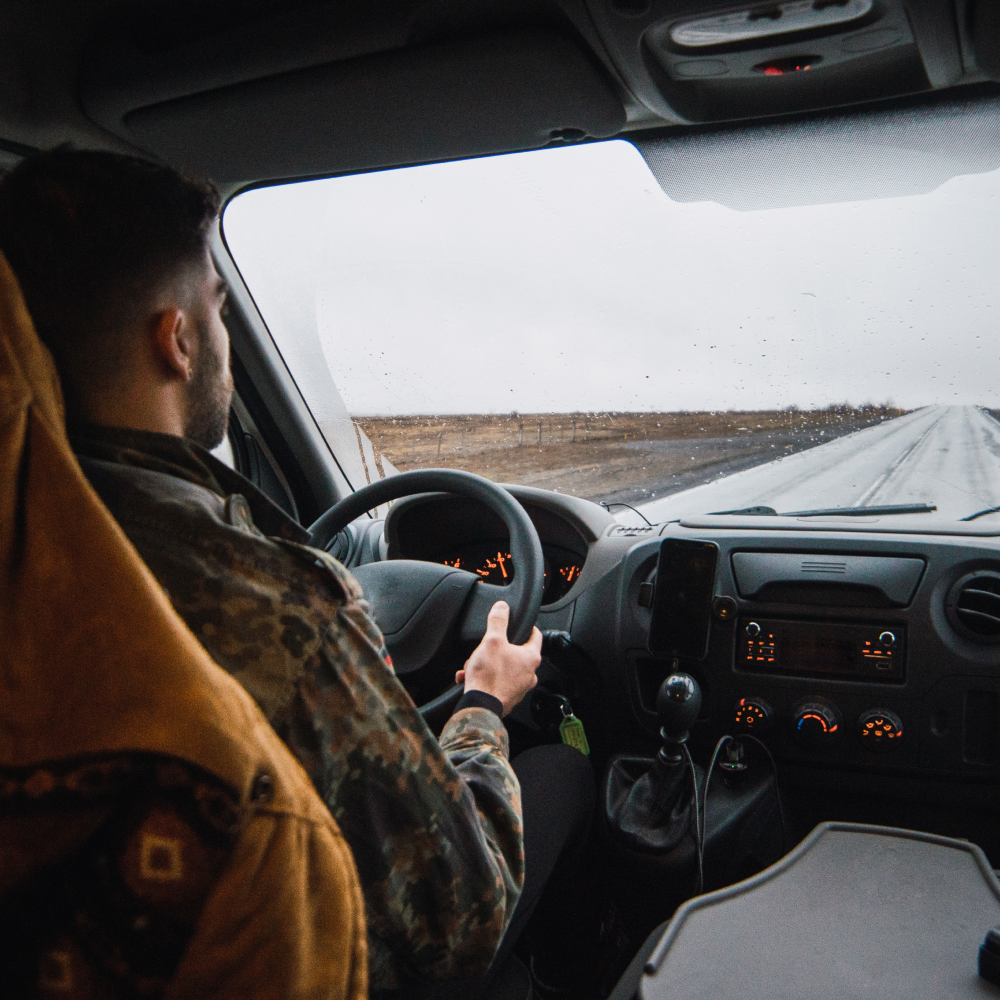 A man in a camouflage jacket is driving a car