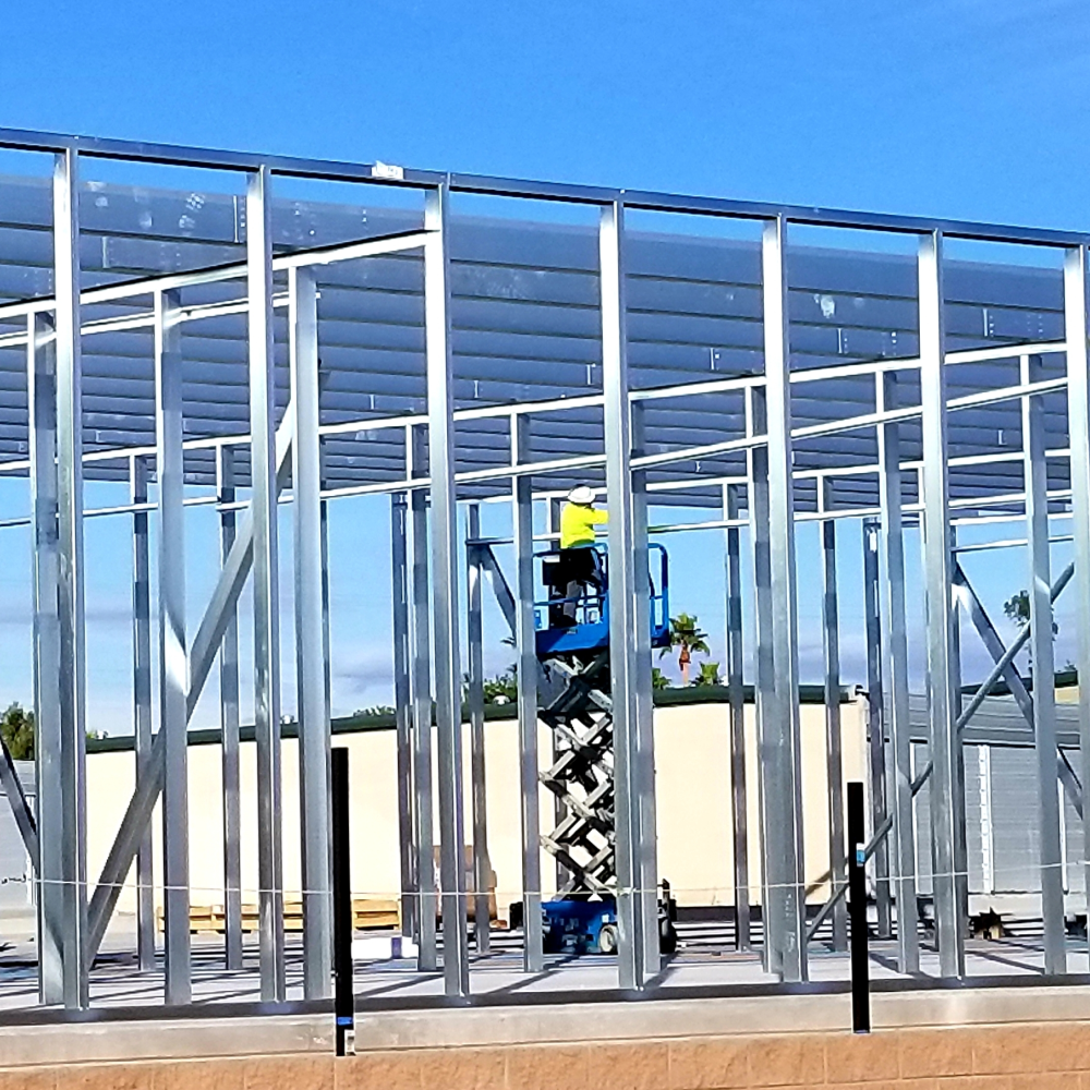 A man is standing on a scissor lift in front of a building under construction.