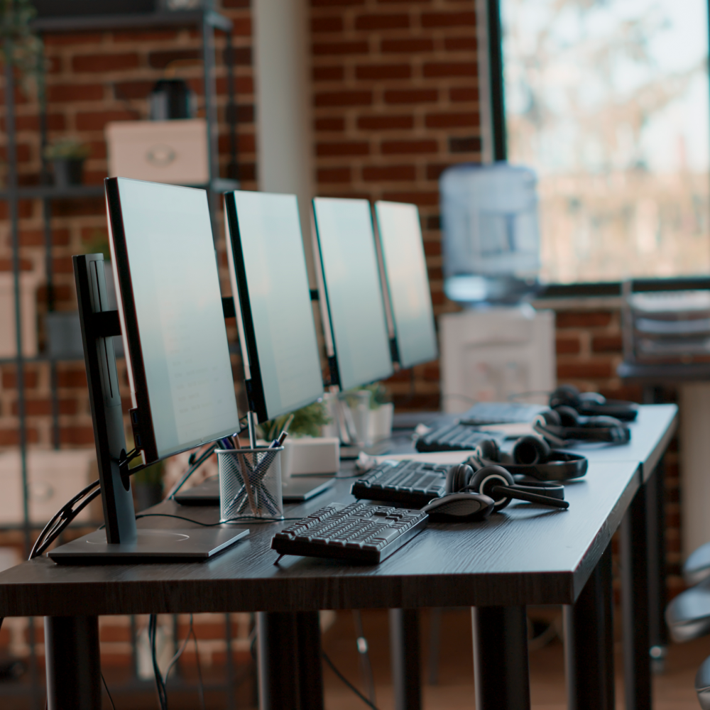 A row of computer monitors and keyboards on a desk in an office.