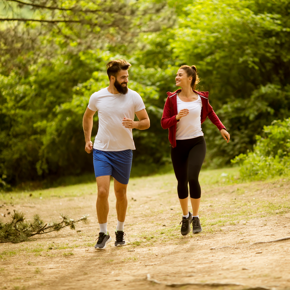 A man and a woman are walking down a dirt path in the woods.