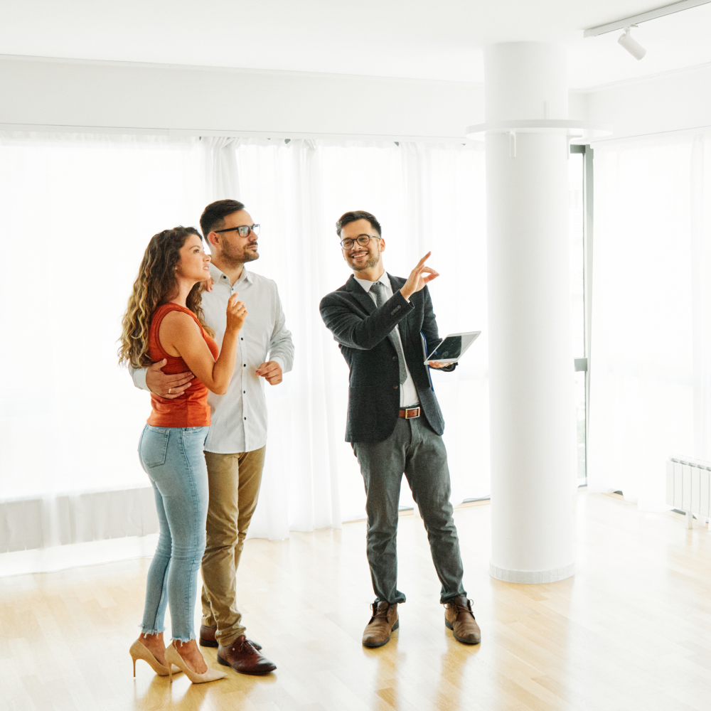 A group of people are standing in an empty room looking at a tablet.